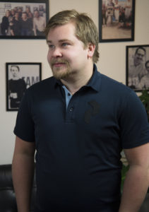 Ung man i profil, står i kontorsmiljö med fotografier på väggarna.