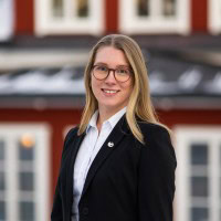 Ung kvinna i professionell klädsel utomhus med stad i bakgrunden.