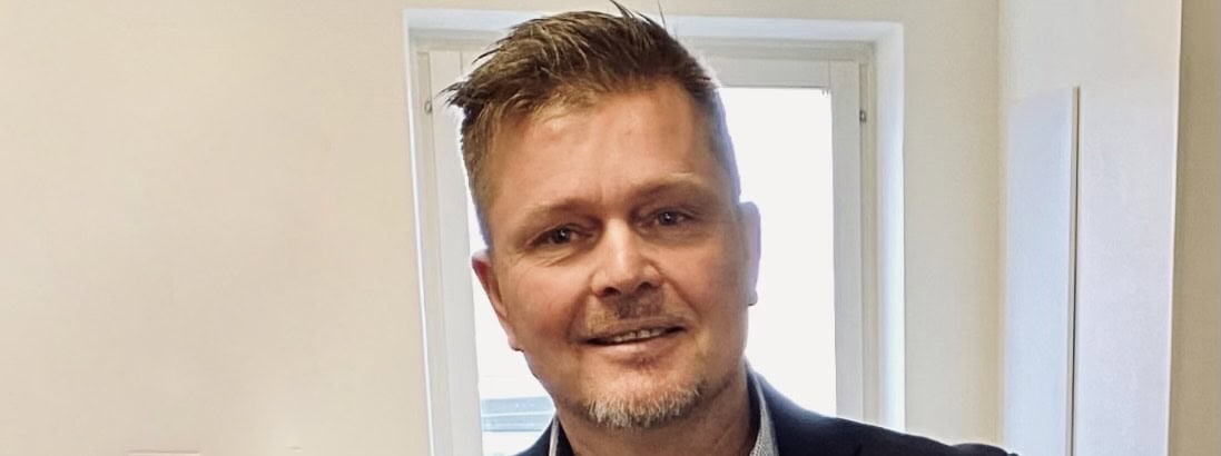 Man i professionell kl&auml;dsel framf&ouml;r f&ouml;nster i kontorsmilj&ouml;.