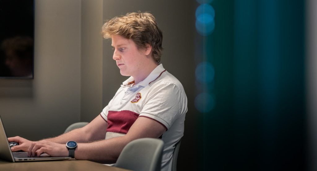 Ung man med laptop, fokuserad på arbete i kontorsmiljö.